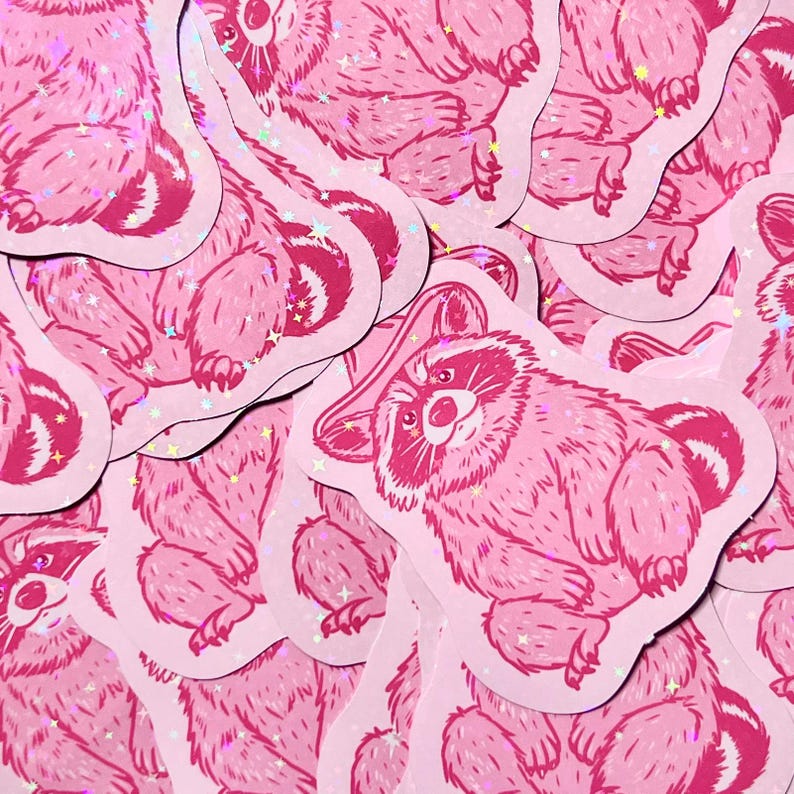 May include: A stack of pink raccoon stickers with a glittery finish. Each sticker features a cartoon raccoon with a playful expression.