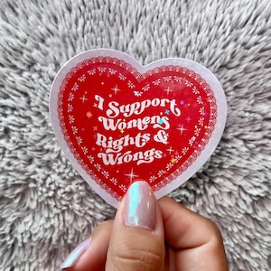 May include: A red heart-shaped sticker with a white border and the text "I Support Women's Rights & Wrongs" in white lettering with glitter accents.