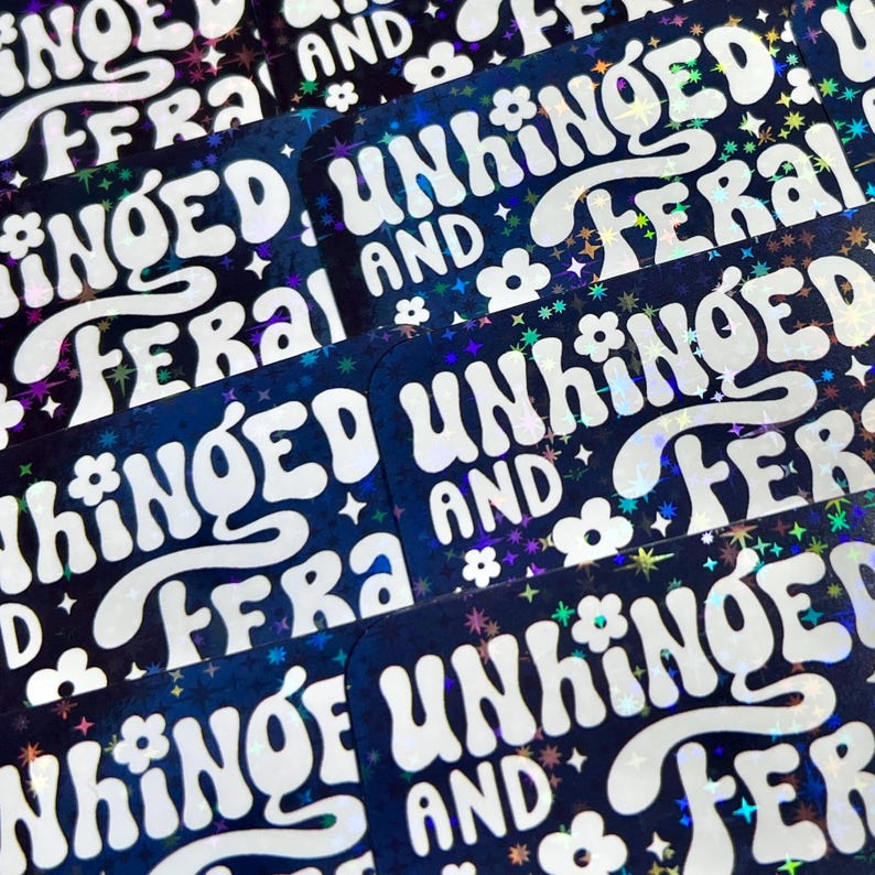 May include: A collection of rectangular stickers with a dark blue background and holographic accents. The stickers feature the words "UNHINGED AND FERAL" in a white, retro font, along with small flower and star graphics.