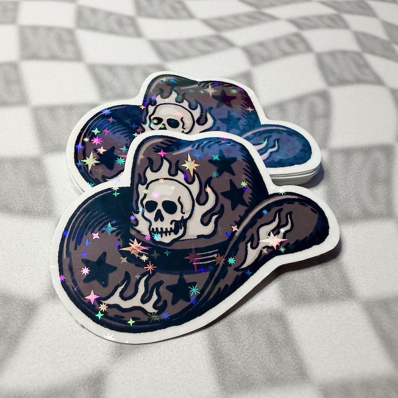 Skull cowboy hat sticker leaning against a stacked pile of matching stickers on a grey checkered background.