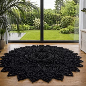 May include: A circular black rug featuring an intricate, raised crochet pattern that radiates from a central medallion to a scalloped, petal-like edge. The thick, textured yarn creates a detailed, symmetrical design across the entire surface.