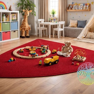 Peut inclure: Un tapis rouge tressé dans une salle de jeux pour enfants. Des jouets, dont un ours en peluche, un train en bois et un camion jaune, sont éparpillés sur le tapis. Une girafe en peluche et un meuble de rangement blanc avec des bacs colorés sont en arrière-plan.