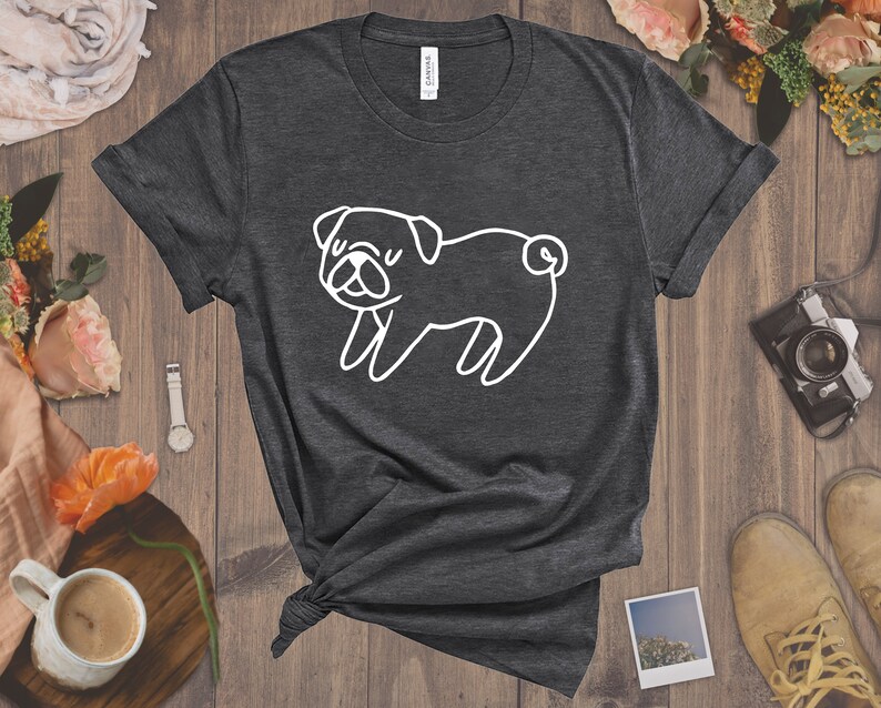 May include: A dark gray t-shirt with a white outline of a pug dog. The pug is facing the left side of the image and has its tongue sticking out.