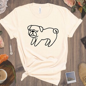 May include: A beige t-shirt with a black line drawing of a pug on the front.