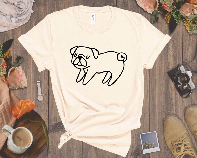 May include: A beige t-shirt with a black line drawing of a pug on the front.