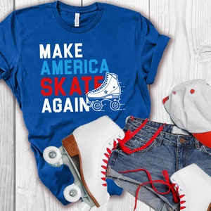 Może przedstawiać: Niebieska koszulka z napisem "Make America Skate Again" białymi literami. Na koszulce widnieje czerwono-biało-niebieska rolka. Koszulka leży na białym drewnianym tle z parą białych rolek, niebieskimi dżinsowymi spodenkami i biało-czerwoną czapką z daszkiem.