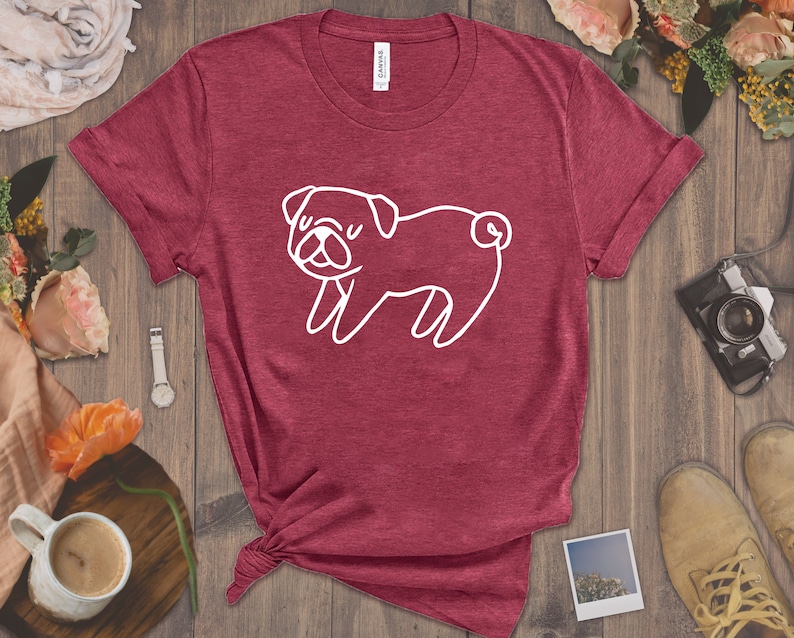 May include: A maroon t-shirt with a white outline of a pug dog. The shirt is made of a soft, comfortable material.