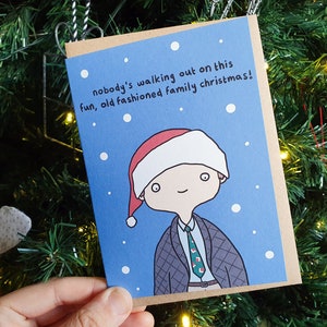 May include: A Christmas card featuring a cartoon illustration of a person wearing a Santa hat and a tie. The text on the card reads "nobody's walking out on this fun, old fashioned family christmas!"