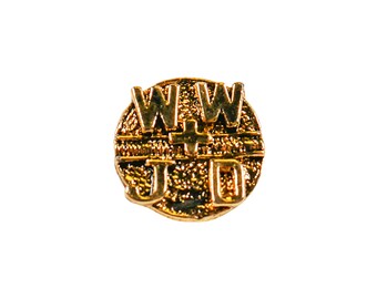 May include: A gold-colored pin with the letters "WWJD" and a cross in the center. The pin has a textured, circular design and is set against a white background. The letters are raised and in a bold font.