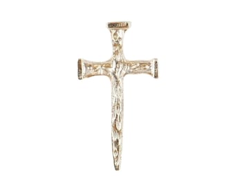 May include: A silver metal cross shaped like a nail. The cross has a detailed design and a pointed tip.