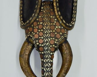This African Babanki tribe elephant mask is hand-carved from wood and embellished with cowrie shells and coins. 34 x 12 x 6