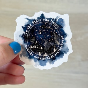 May include: A white sticker with a watercolor-style background of a dark blue night sky with stars, a crescent moon, and a mountain range. The text "To the stars who listen and the dreams that are answered" is written in a circle around the image.