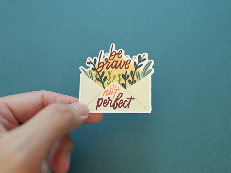 May include: A white envelope sticker with green and yellow floral illustrations and the text "be brave not perfect".