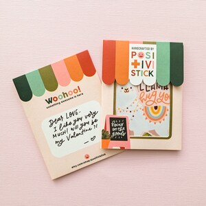 May include: Two colorful cards with a llama and a handwritten message. The llama card says "llama hug you" and the other card says "Dear Love... I like you very much! Will you be my Valentine?!". Both cards have a rainbow and a sign that says "focus on the goods".