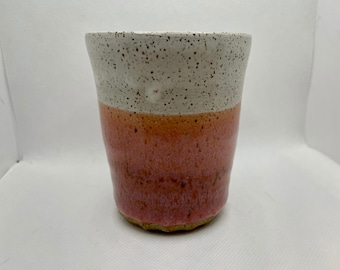May include: A white ceramic mug with a speckled glaze and a pink and orange glaze on the bottom half.