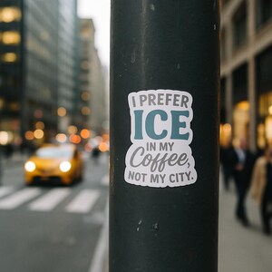 May include: A sticker on a black pole with the text "I PREFER ICE IN MY Coffee, NOT MY CITY." The sticker has a white background with blue and gray text. The background shows a city street with a yellow taxi.