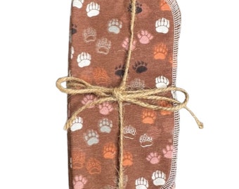 May include: A bundle of brown fabric squares featuring a repeating paw print pattern in white, pink, grey, and orange. The bundle is tied with twine. The fabric has a white stitched border.