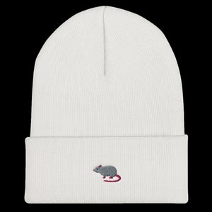 Könnte beinhalten: Weiße Strickmütze mit einem kleinen gestickten grauen Ratte mit einem rosafarbenen Schwanz.