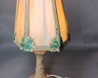Pode incluir: Um abajur de mesa vintage com um abajur hexagonal de vidro fosco com detalhes florais verdes. A base do abajur é feita de ferro fundido e tem um acabamento creme.