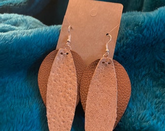 Peut inclure: Une paire de boucles d'oreilles pendantes à deux couches de cuir. La couche supérieure est brune et la couche inférieure est beige clair. Les boucles d'oreilles sont suspendues à des crochets argentés.