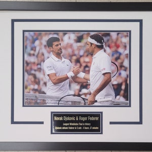 May include: A framed photograph of two tennis players, Novak Djokovic and Roger Federer, shaking hands on a tennis court. The caption below the photo reads "Novak Djokovic & Roger Federer Longest Wimbledon Final in History Djokovic defeats Federer in 5 sets - 4 hours, 57 minutes".