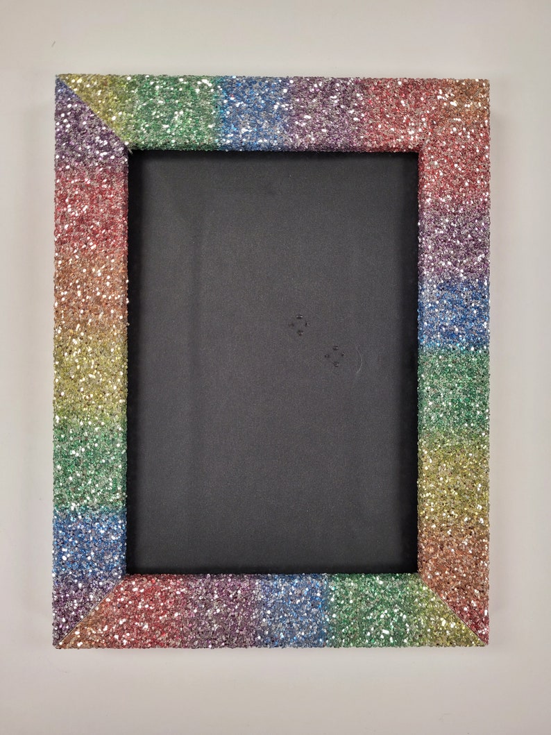 May include: A rainbow glitter picture frame with a black background. The frame is made of cardboard and has a rainbow glitter finish.