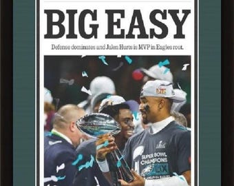 May include: Framed Philadelphia Inquirer newspaper front page with the headline "BIG EASY" and a photo of the Super Bowl LIX champions. The image shows players holding the trophy, with confetti falling. The frame is black.