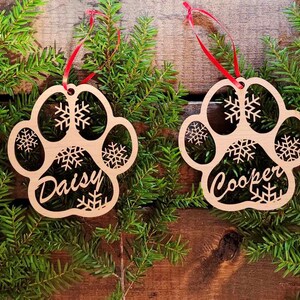 May include: Four wooden paw print ornaments with snowflakes and the names Max, Daisy, Cooper, and Honey.