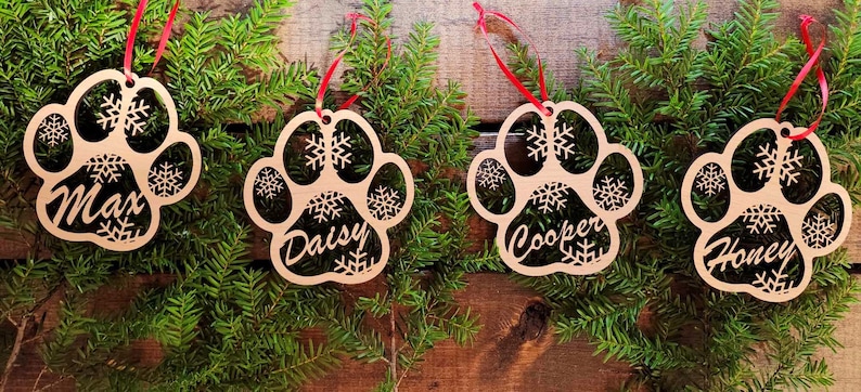 May include: Four wooden paw print ornaments with snowflakes and the names Max, Daisy, Cooper, and Honey.