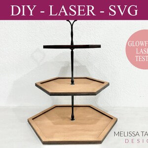 Op de afbeelding: Een tweelaagse houten zeshoekige serveerstandaard met een zwarte metalen staaf en dwarsbalk. De standaard is lasergesneden en getest voor gebruik met een Glowforge lasersnijder.  DIY - LASER - SVG