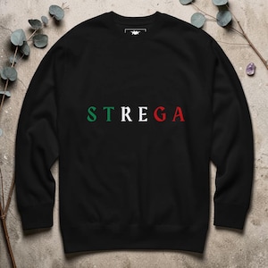 May include: Black crew neck sweatshirt with the word "STREGA" printed across the chest in green, white, and red. The sweatshirt is made of a soft material. The design is simple and bold, with the text in a clean, sans-serif font.