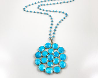 May include: A turquoise gemstone necklace with a large pendant made of multiple turquoise stones arranged in a circular pattern.