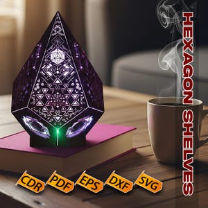 May include: A geometric, purple lamp with detailed cut-out patterns, placed on a pink book. The lamp emits a green light from its base. A coffee mug and the text "HEXAGON SHELVES" are also visible.