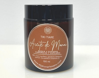 Op de afbeelding: Een bruine glazen pot met een zwarte deksel die Tiki Tiare Aceite de Monoï lichaams- en haarolie bevat. Het etiket is bruin met zilveren tekst en een zilveren knoopontwerp. Het etiket vermeldt "Tiki Tiare Aceite de Monoï", "Masaje y Cuidados Corporales y Capilares", "INCI: Coco nucifera, gardenia tahitensis, parfum, tocopherol (vitamine E)", "100 ml" en "www.eljabonartesano.com".