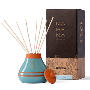 Op de afbeelding: Een blauwe keramische diffuserfles met een terracotta deksel en houten stokjes. De fles heeft een gouden label met de tekst "KAHE NA COLLECTION" en "DIFUSOR BRISA DEL MAR".