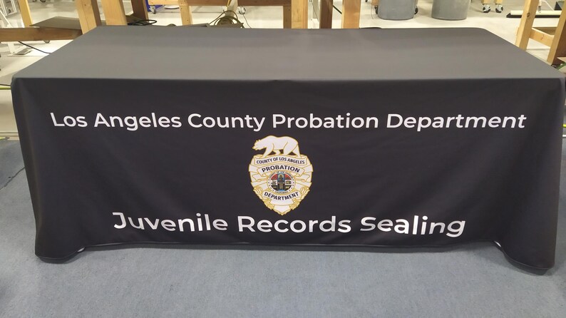 May include: Black table cover with white text that reads "Los Angeles County Probation Department" and "Juvenile Records Sealing". A gold badge with a bear and the words "County of Los Angeles Probation Department" is in the center of the table cover.