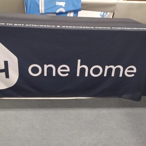 May include: A dark blue table cover with the text "Ask me how to get affordable & accessible home maintenance" and the logo "One Home" with a white house icon and the letter "H" inside.