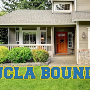 May include: A blue and gold UCLA Bound yard sign on a green lawn in front of a house.