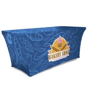 May include: Blue table cover with a bakery shop logo featuring a cupcake, crossed rolling pins, and the text "Bakery Shop - Premium Quality". The background pattern includes various bakery items like bread, croissants, and wheat.