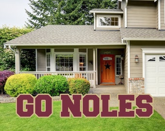 May include: A maroon and gold "GO NOLES" yard sign with large block letters. The sign is on a green lawn in front of a house.