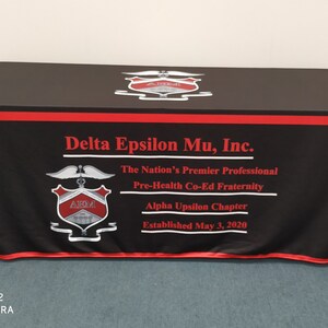 May include: Black table cover with red trim and a white logo that says "Delta Epsilon Mu, Inc." The Nation's Premier Professional Pre-Health Co-Ed Fraternity Alpha Upsilon Chapter Established May 3, 2020
