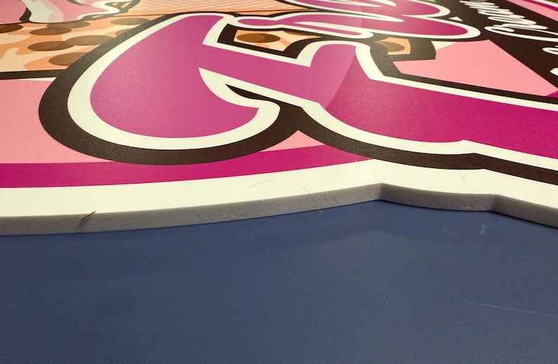 May include: A pink and white foam board with a pink and black graphic of the word "Foo" with a white outline. The board is sitting on a blue surface.