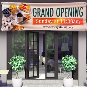 May include: A banner announcing a grand opening of a restaurant or cafe. The banner is beige with orange text and features a breakfast scene with coffee, pastries, and fruit. The text reads "Grand Opening, Sunday at 11:00am, www.eateryatmail.com".