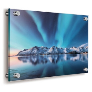 Op de afbeelding: Een rechthoekige acryl wandprint met een levendige nachtelijke hemel met blauwe en groenblauwe noorderlichten boven besneeuwde bergen en een kalm meer. De print is bevestigd met vier zilverkleurige metalen afstandhouders op de hoeken.