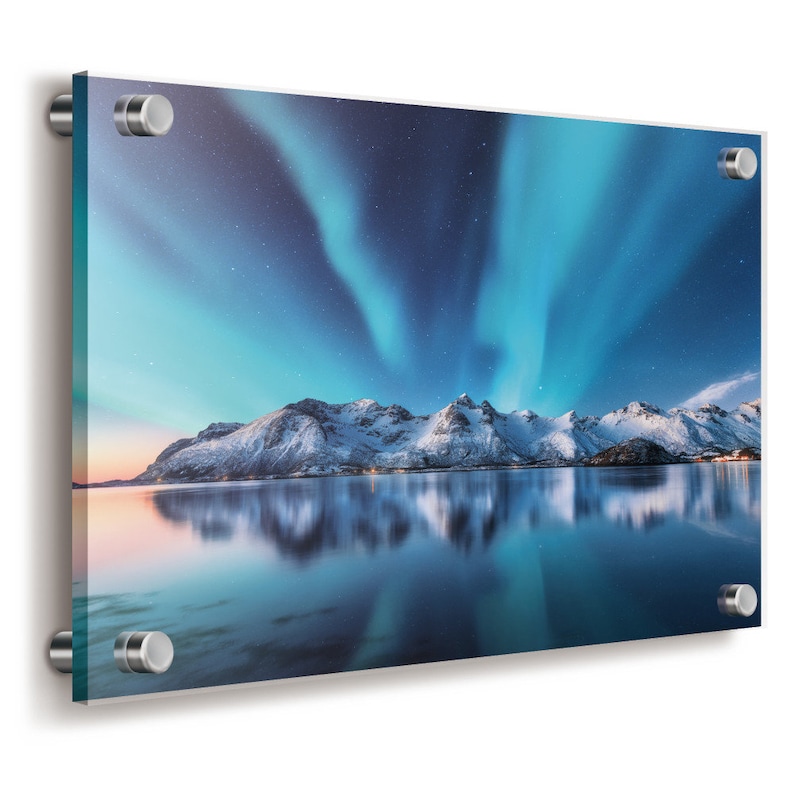 Op de afbeelding: Een rechthoekige acryl wandprint met een levendige nachtelijke hemel met blauwe en groenblauwe noorderlichten boven besneeuwde bergen en een kalm meer. De print is bevestigd met vier zilverkleurige metalen afstandhouders op de hoeken.