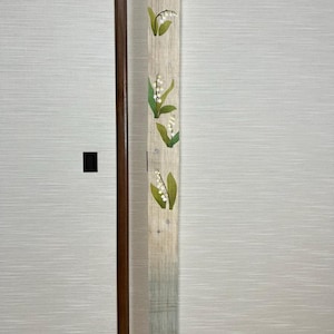 Può includere: Un pannello di tessuto bianco e verde con un disegno di fiori di mughetto. Il pannello è appeso a una parete bianca.