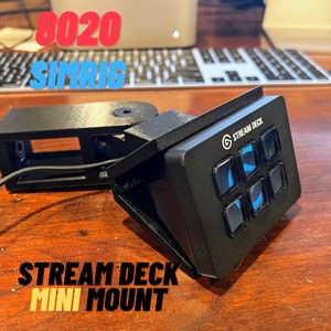 May include: A black Stream Deck Mini mount with the text "STREAM DECK MINI MOUNT" printed in yellow. The mount is attached to a black Stream Deck Mini with blue buttons and the text "STREAM DECK" printed in white.