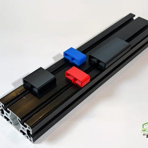 May include: A black aluminum extrusion with several colored plastic components. The components are black, red, and blue. The extrusion has a channel design. The image is taken from a high angle.