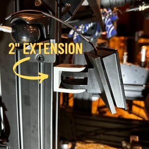 May include: A black 2" extension for a 3D printer. The extension is made of plastic and has a metal hinge. The extension is attached to a black metal pole.