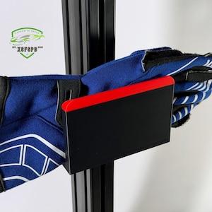 May include: Blue and white racing gloves held by a black and red bracket. The gloves are made of a soft material and have white accents. The bracket is mounted on a black metal frame. The image also includes a logo with the text "XFSFSPD".